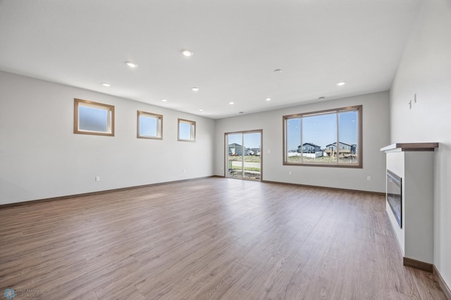 unfurnished living room featuring light wood-type flooring, baseboards, recessed lighting, and a glass covered fireplace