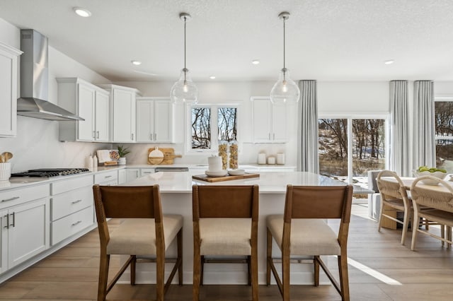 2704 Aspen Dr, Shakopee, MN 55379 - kitchen featuring wall chimney range hood, stainless steel gas cooktop, light countertops, a kitchen bar, and a kitchen island