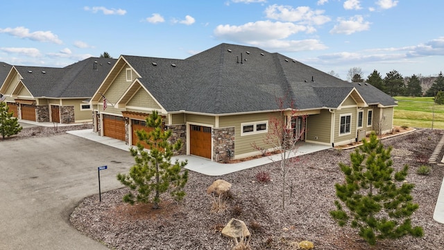back of house with roof with shingles, driveway, and stone siding