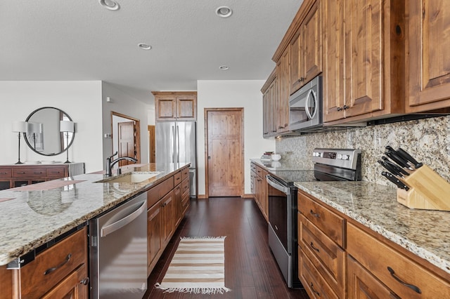 kitchen with brown cabinets, light stone counters, a sink, appliances with stainless steel finishes, and backsplash