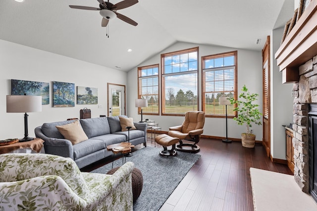living room featuring dark wood-style flooring, ceiling fan, a stone fireplace, baseboards, and lofted ceiling