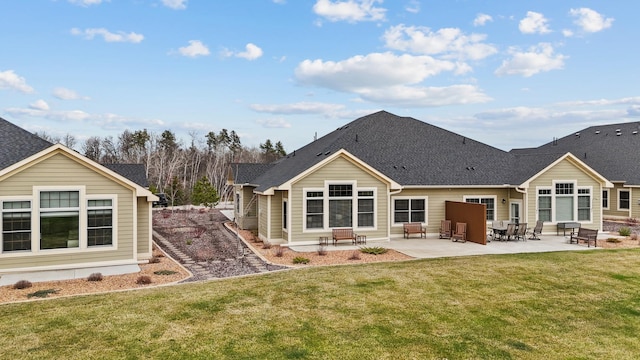 rear view of property featuring a lawn, roof with shingles, and a patio area