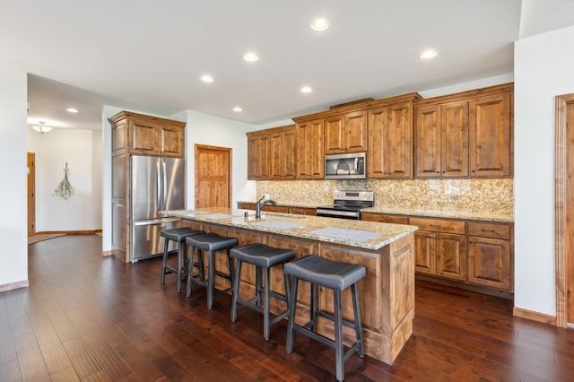 7466 Fairway Ln, Breezy Point, MN 56472 - kitchen with appliances with stainless steel finishes, brown cabinets, decorative backsplash, a breakfast bar, and an island with sink