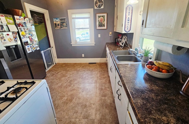 822 4th Ave, Madison, MN 56256 - kitchen featuring dark countertops, a sink, baseboards, stainless steel fridge, and white cabinetry