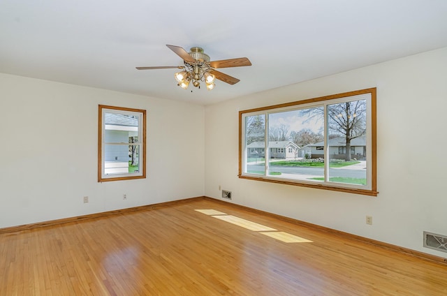 empty room with visible vents, a ceiling fan, light wood-style flooring, and baseboards