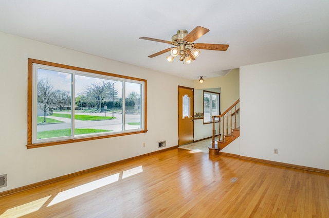unfurnished living room with visible vents, stairs, light wood-style floors, baseboards, and ceiling fan