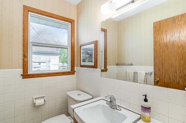 half bathroom featuring a sink, toilet, wallpapered walls, and a wealth of natural light