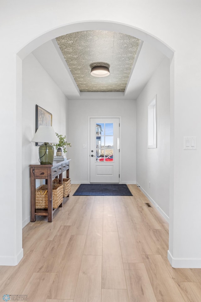 entryway featuring arched walkways, baseboards, and light wood finished floors