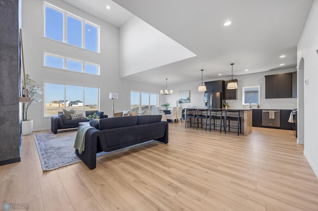 living room featuring a chandelier, light wood-style flooring, recessed lighting, baseboards, and a towering ceiling