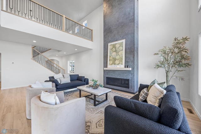 living area with visible vents, a towering ceiling, a large fireplace, wood finished floors, and stairs