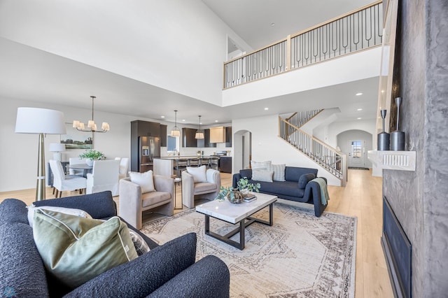 living room with a towering ceiling, arched walkways, a fireplace, stairway, and light wood finished floors