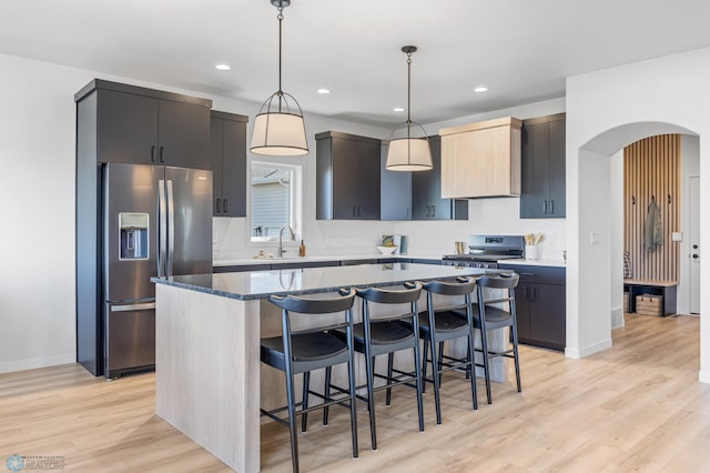 kitchen with a sink, a kitchen breakfast bar, stainless steel appliances, light wood-type flooring, and a kitchen island