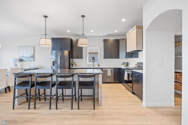 kitchen with a breakfast bar area, a kitchen island, a sink, stainless steel appliances, and light wood-style flooring
