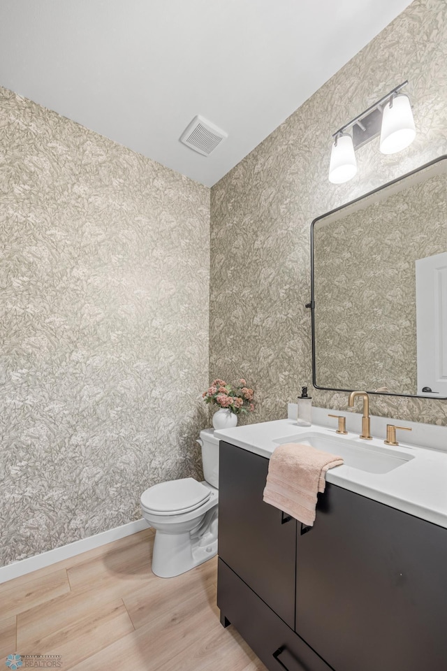 bathroom with vanity, toilet, wallpapered walls, baseboards, and visible vents