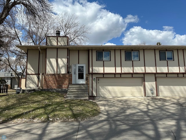 split foyer home featuring driveway, a chimney, a garage, brick siding, and stucco siding