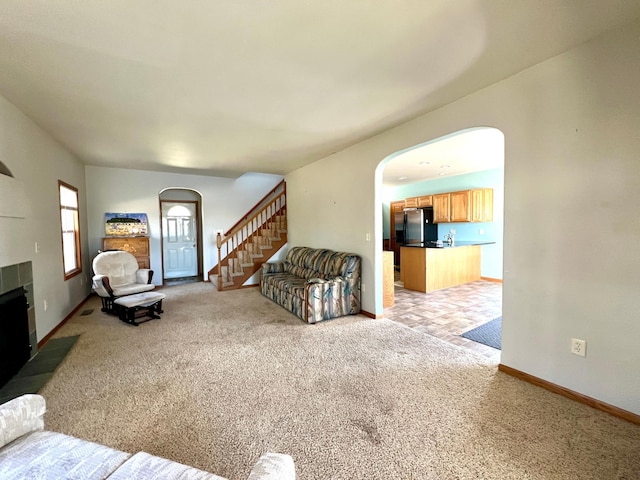 living area with light colored carpet, a tiled fireplace, arched walkways, stairway, and baseboards