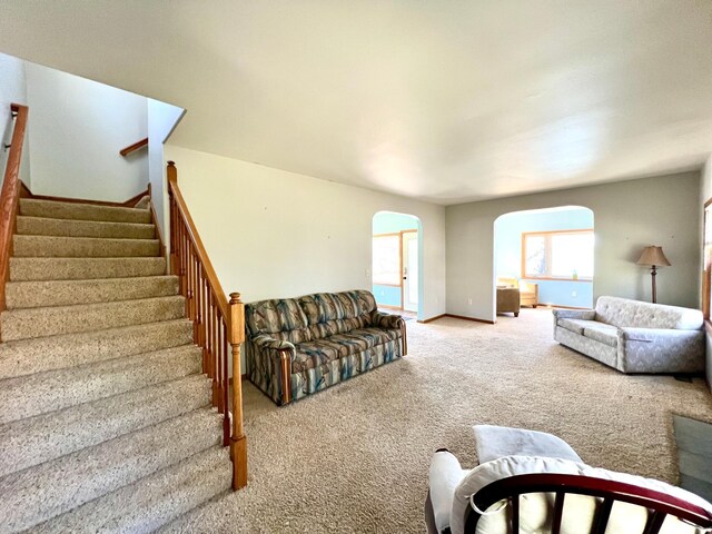 living room featuring baseboards, arched walkways, carpet, and stairs
