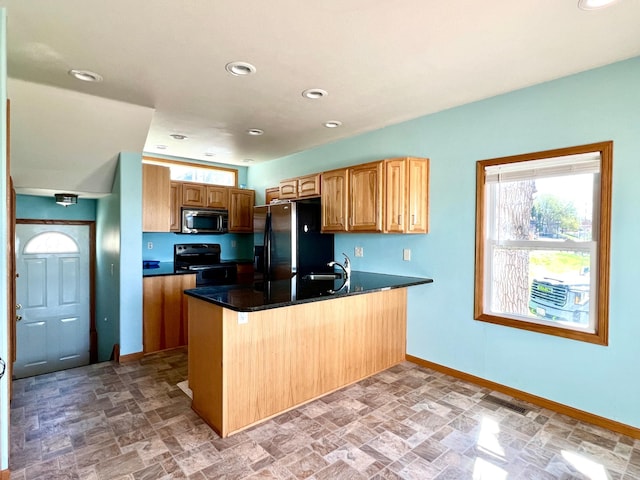 kitchen featuring a peninsula, plenty of natural light, stone finish floor, and black appliances