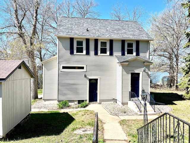 view of front of home featuring roof with shingles, an outbuilding, a storage shed, and a front yard