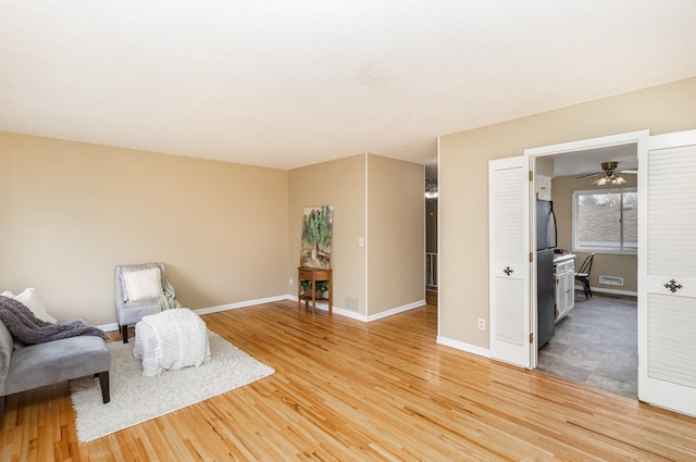 living area featuring a ceiling fan, baseboards, and light wood-type flooring