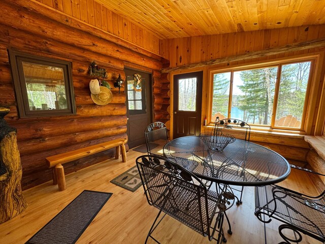 dining space with log walls, wood ceiling, and wood finished floors
