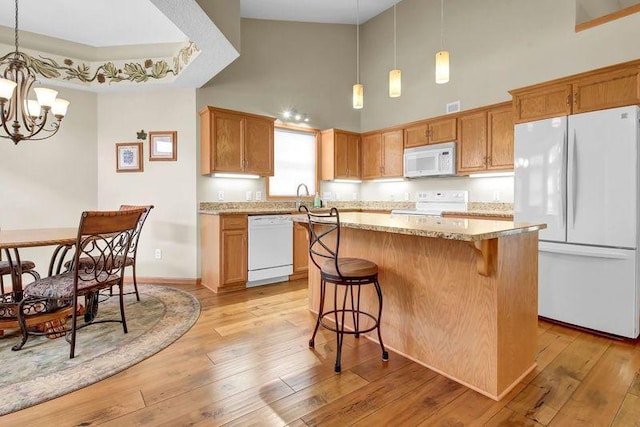 kitchen featuring white appliances, a high ceiling, a chandelier, a kitchen island, and light stone countertops