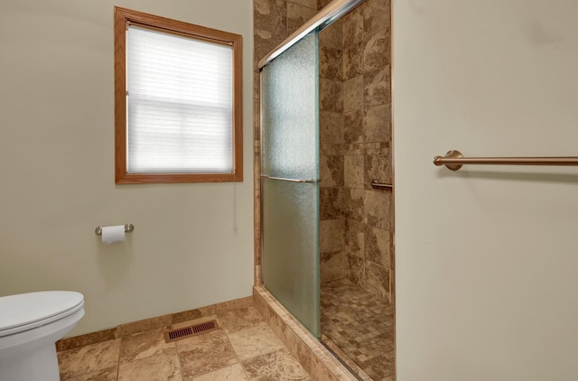 full bath featuring a stall shower, toilet, baseboards, and stone finish floors