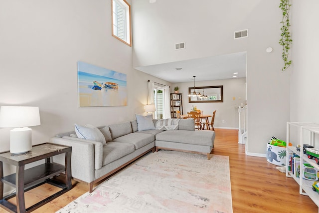 living area with an inviting chandelier, visible vents, light wood-style flooring, and a towering ceiling