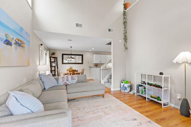 living room with visible vents, stairs, a towering ceiling, light wood-style floors, and a notable chandelier