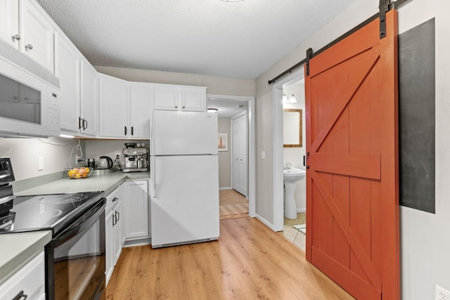 kitchen featuring a barn door, light countertops, light wood finished floors, white appliances, and white cabinetry