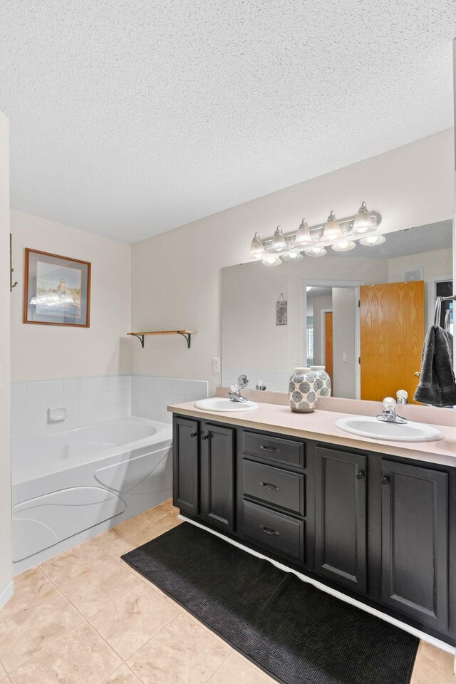 full bathroom with tile patterned flooring, double vanity, a textured ceiling, a bath, and a sink