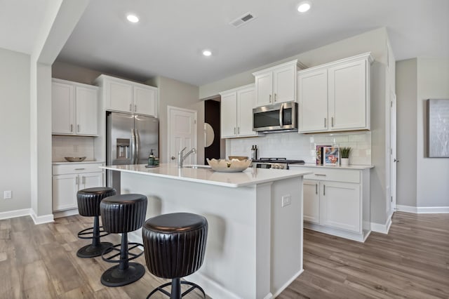 kitchen with visible vents, decorative backsplash, wood finished floors, a kitchen breakfast bar, and stainless steel appliances