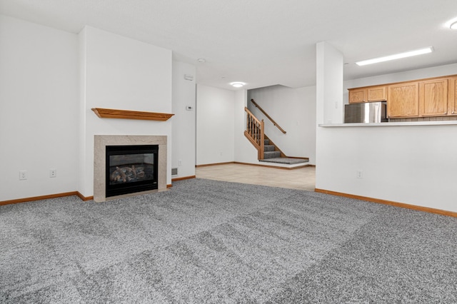 unfurnished living room featuring a fireplace with flush hearth, baseboards, carpet flooring, and stairs