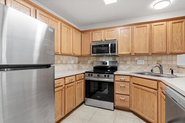 kitchen featuring light tile patterned flooring, appliances with stainless steel finishes, a sink, light countertops, and decorative backsplash