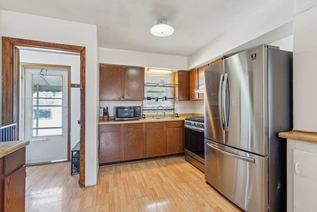 kitchen with appliances with stainless steel finishes, a sink, light countertops, light wood-style floors, and brown cabinetry
