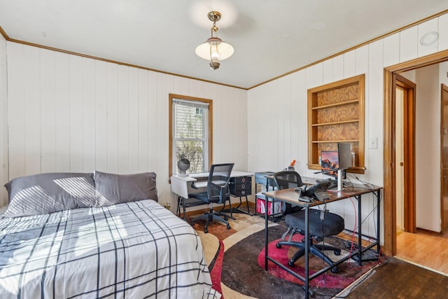 bedroom featuring ornamental molding, wood finished floors, a desk, and wood walls
