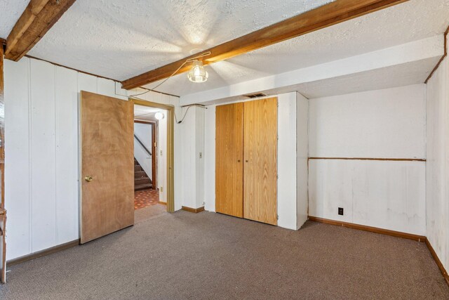 unfurnished bedroom featuring carpet, beamed ceiling, a textured ceiling, and baseboards