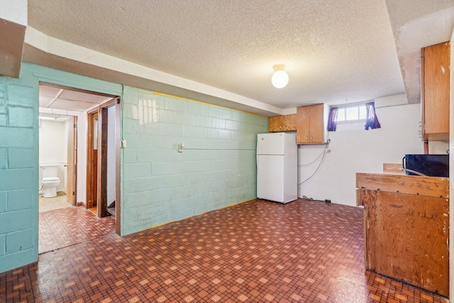 basement with freestanding refrigerator, concrete block wall, and a textured ceiling