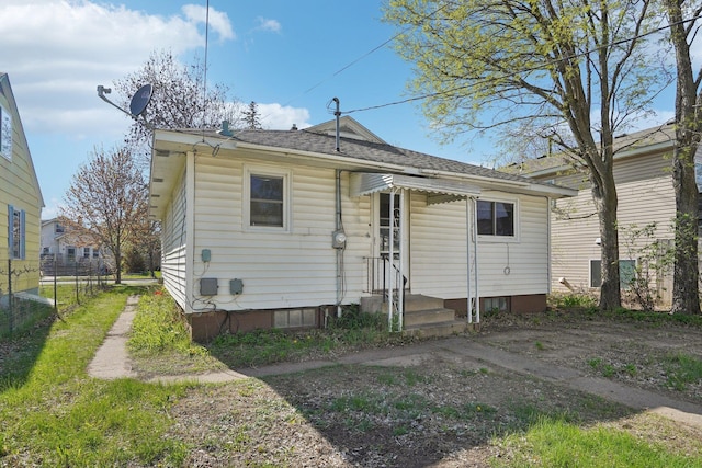 back of house with entry steps, roof with shingles, and fence