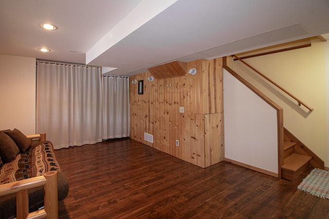 unfurnished living room featuring dark wood finished floors, stairs, wood walls, and baseboards