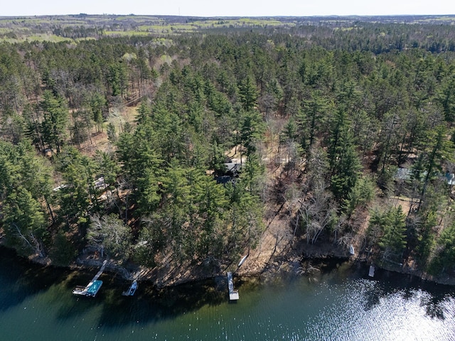aerial view of property and surrounding area featuring a heavily wooded area and a nearby body of water