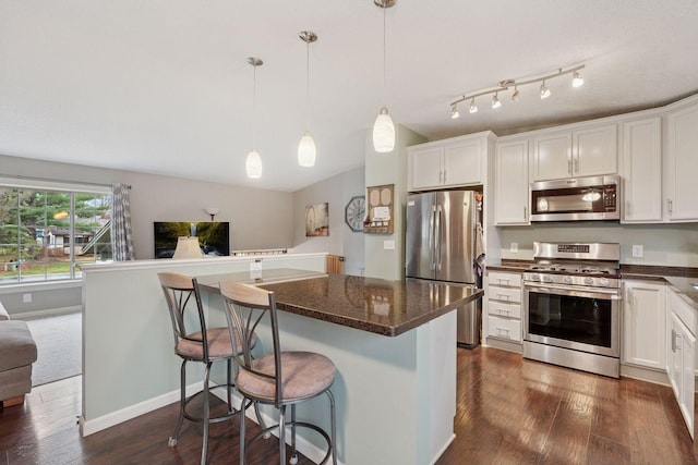 kitchen featuring a breakfast bar area, stainless steel appliances, decorative light fixtures, white cabinetry, and dark wood-type flooring