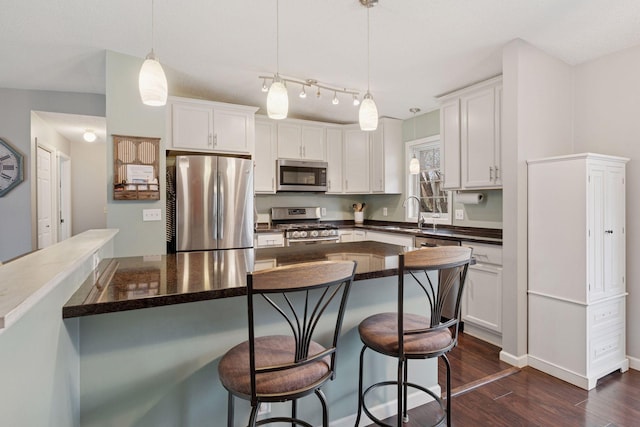kitchen with dark countertops, dark wood-type flooring, white cabinets, a sink, and appliances with stainless steel finishes