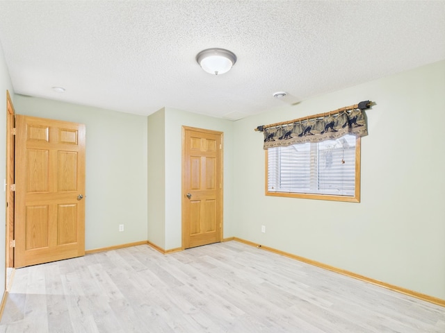 unfurnished bedroom with a textured ceiling, baseboards, and wood finished floors