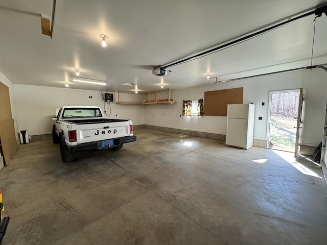 garage featuring baseboards, a garage door opener, and freestanding refrigerator