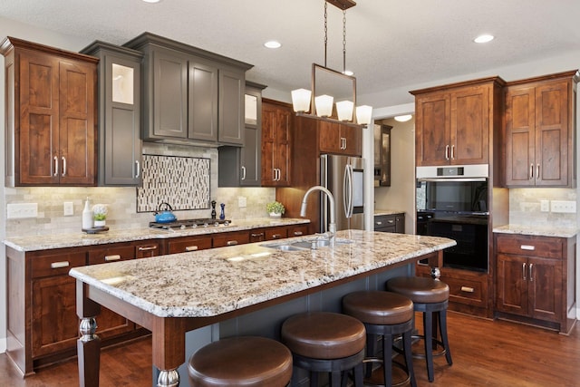 kitchen with a breakfast bar, a sink, dark wood finished floors, backsplash, and stainless steel appliances