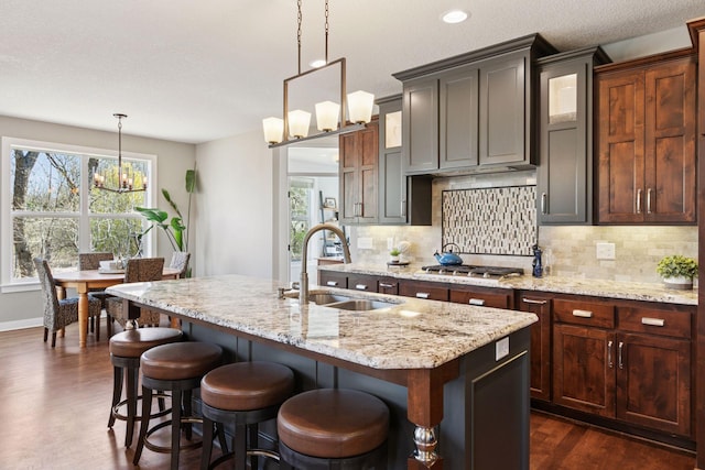 kitchen with stainless steel gas stovetop, tasteful backsplash, a sink, an inviting chandelier, and an island with sink