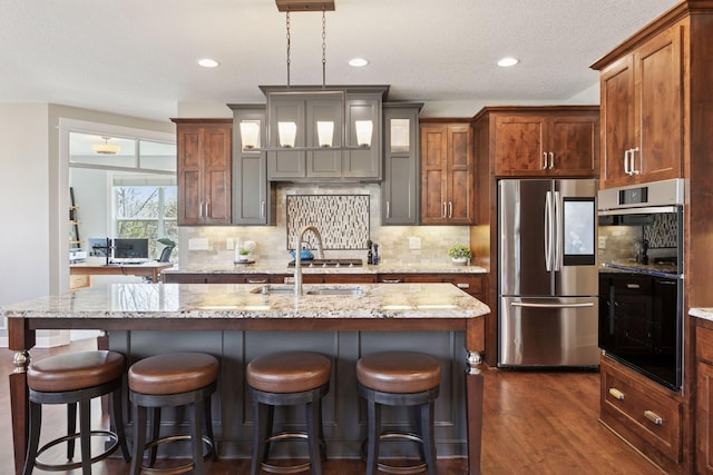 kitchen featuring decorative backsplash, dark wood-style flooring, a kitchen island with sink, light stone countertops, and stainless steel appliances