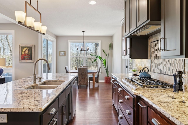 kitchen featuring light stone counters, a sink, a chandelier, dark wood finished floors, and tasteful backsplash
