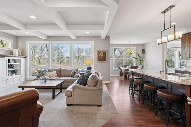 living area with a chandelier, beamed ceiling, dark wood finished floors, and a healthy amount of sunlight